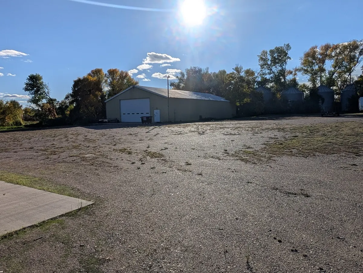 The gravel storage lot at Ben's Farm in late September, with a tan steel shop building, trees turning yellow and grain bins behind it